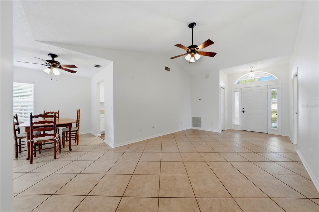 An open-concept living and dining area features white walls, tile flooring, and two ceiling fans — 3828 HOLLOW OAK PLACE, LAND O LAKES, FL