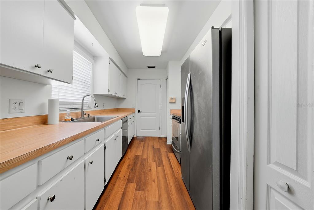A galley kitchen features white cabinets, wood countertops, stainless steel appliances, and wood-look flooring — 3828 HOLLOW OAK PLACE, LAND O LAKES, FL