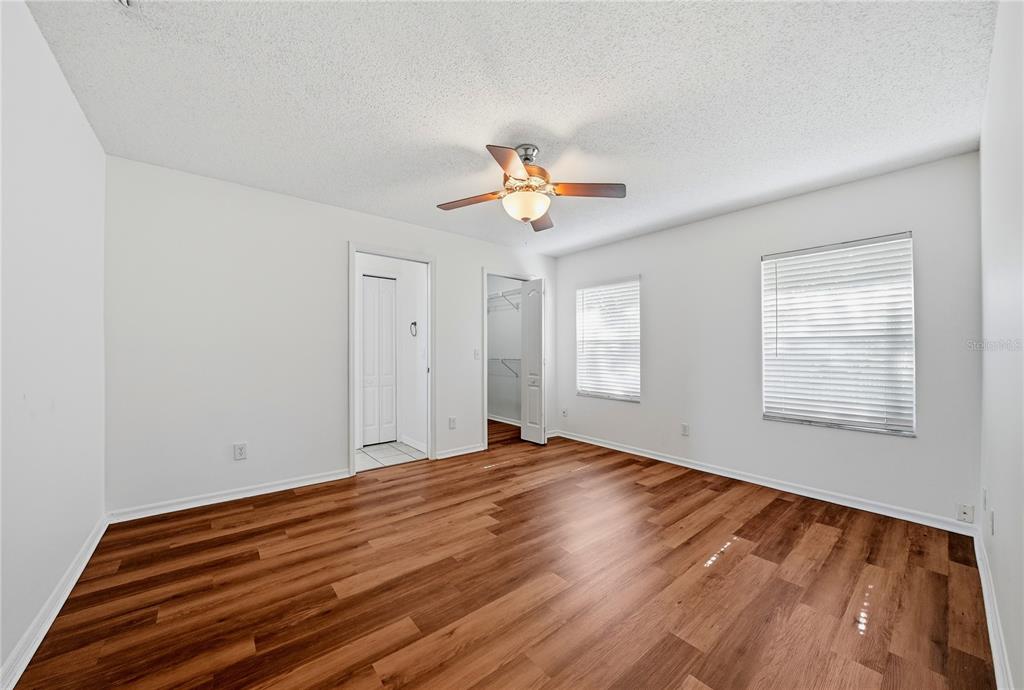 An empty bedroom features white walls, wood-look flooring, a ceiling fan, and two open closets — 3828 HOLLOW OAK PLACE, LAND O LAKES, FL