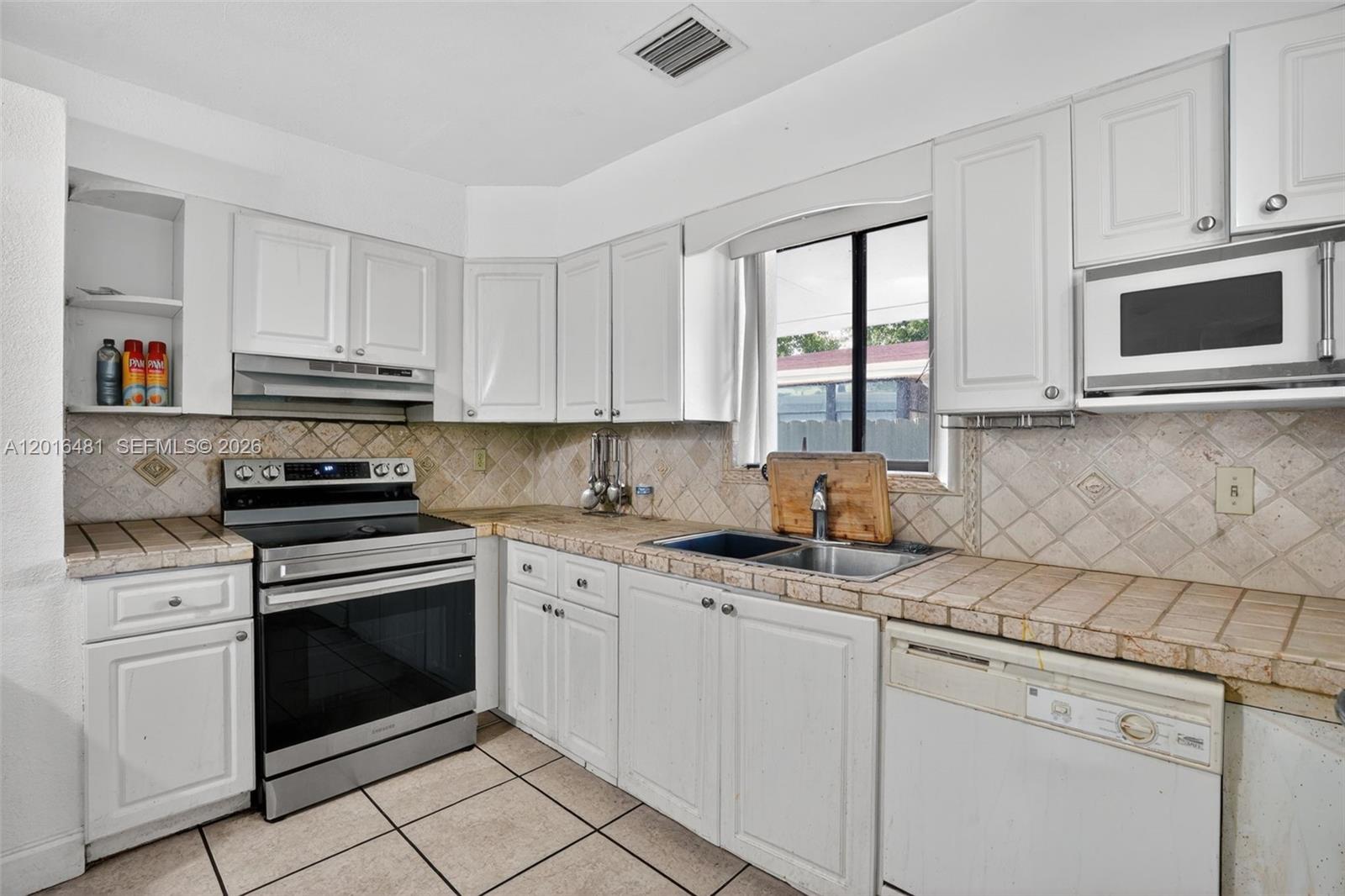A kitchen features white cabinets, stainless steel appliances, and tan tiled countertops and flooring — 2451 NW 11th St, Miami FL 33125, MIAMI, FL
