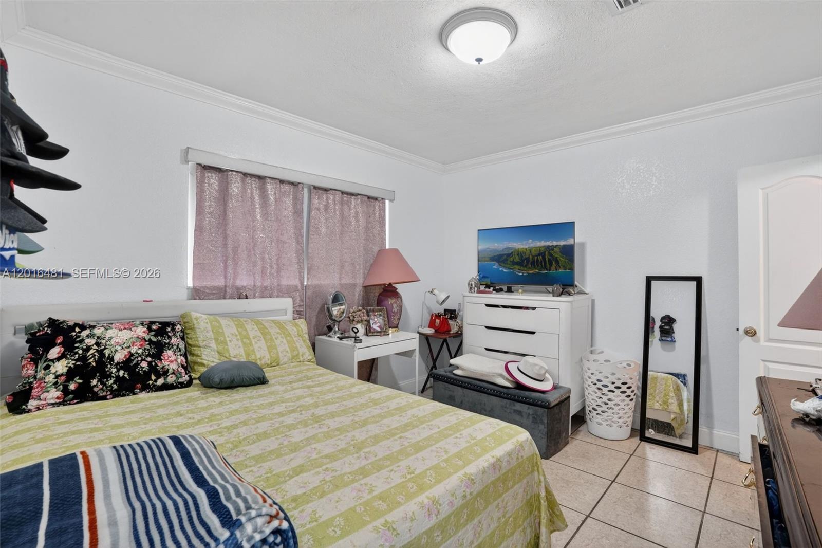 A bedroom features a bed with floral and striped bedding, a white dresser, and tile flooring — 2451 NW 11th St, Miami FL 33125, MIAMI, FL