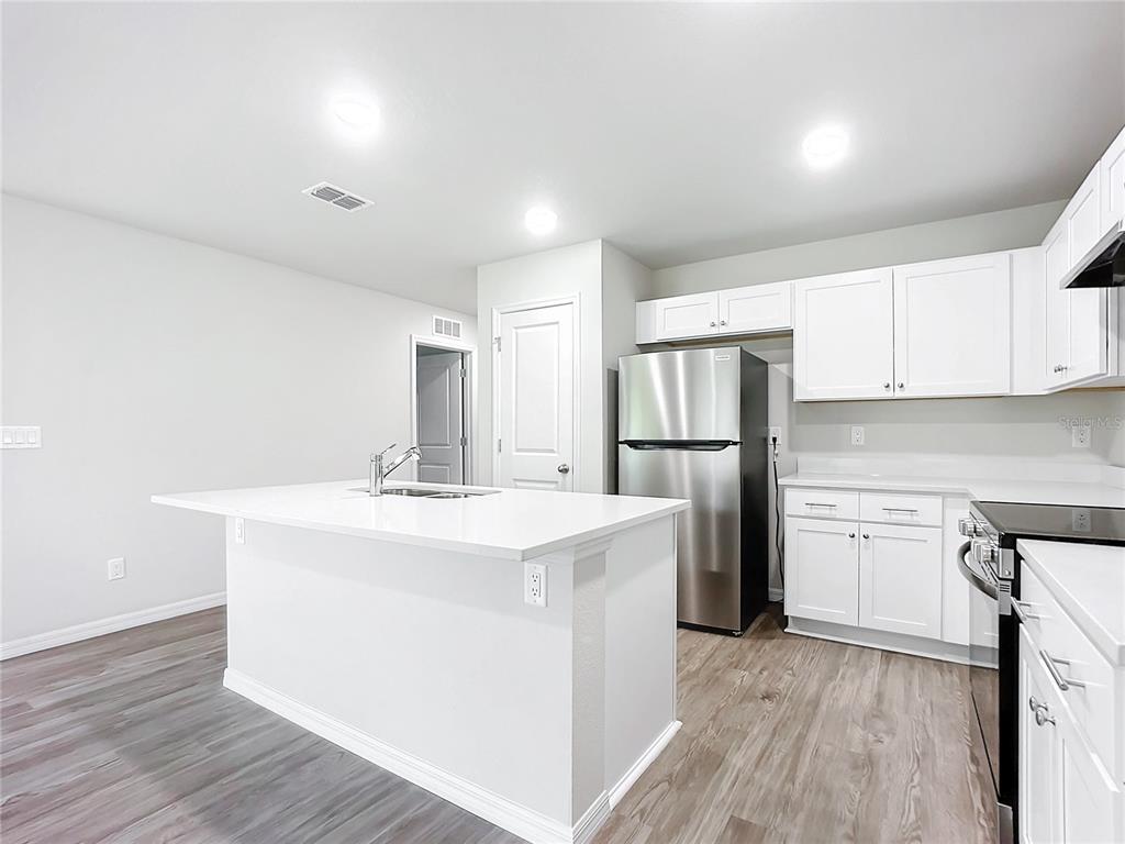 A modern kitchen features white cabinets, stainless steel appliances, and a central island — 38 SLUMBER MEADOW TRAIL, PALM COAST, FL