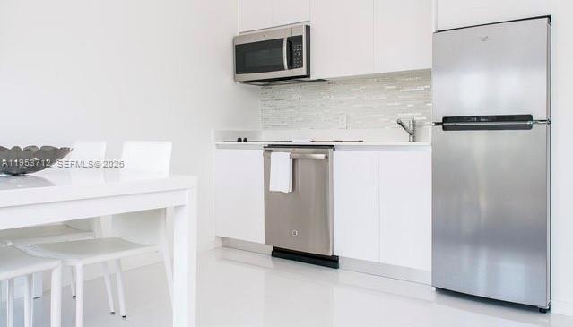 A modern kitchen features white cabinets, stainless steel appliances, and a white dining table — 801 15th St # 208, Miami Beach FL 33139, MIAMI BEACH, FL