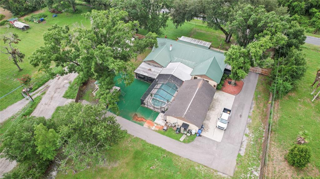 An aerial view shows a house with a green metal roof, pool enclosure, and driveway — 7410 PIERCE HARWELL ROAD, PLANT CITY, FL