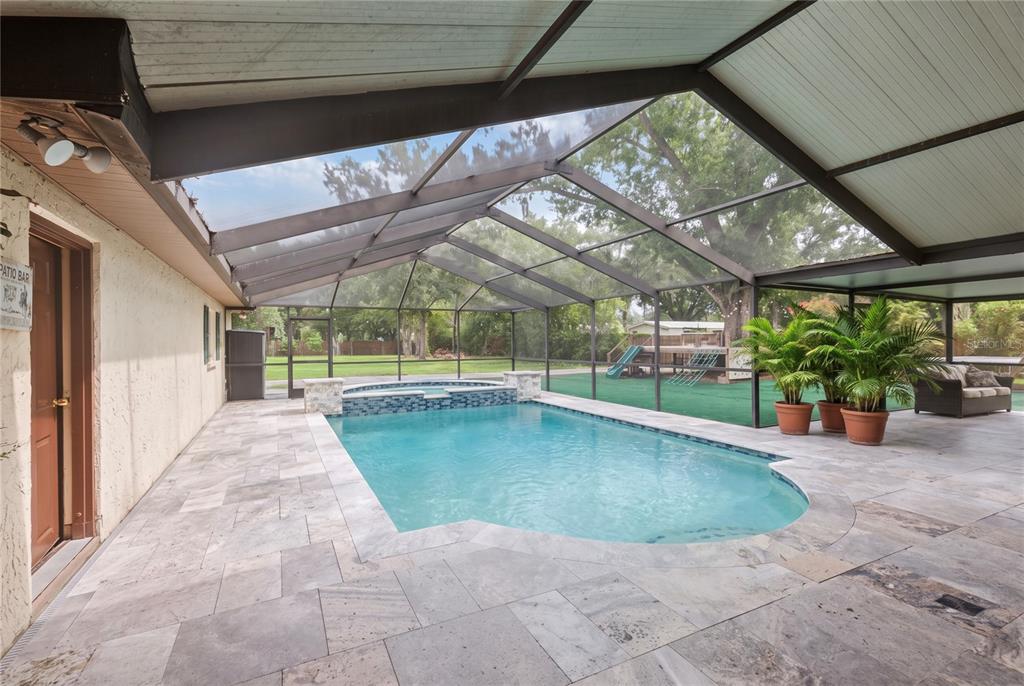 A screened-in patio features a swimming pool, a hot tub, and stone tile flooring — 7410 PIERCE HARWELL ROAD, PLANT CITY, FL