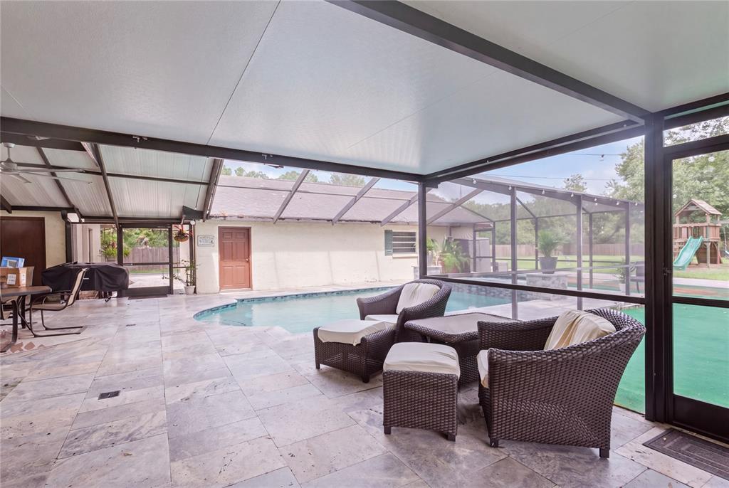 A covered patio with stone flooring overlooks a swimming pool enclosed by a screen — 7410 PIERCE HARWELL ROAD, PLANT CITY, FL