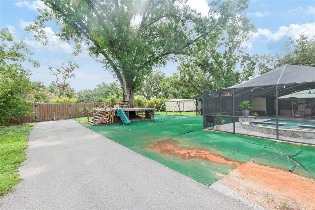 A backyard features a paved driveway, a wooden deck around a tree, and a screened pool — 7410 PIERCE HARWELL ROAD, PLANT CITY, FL