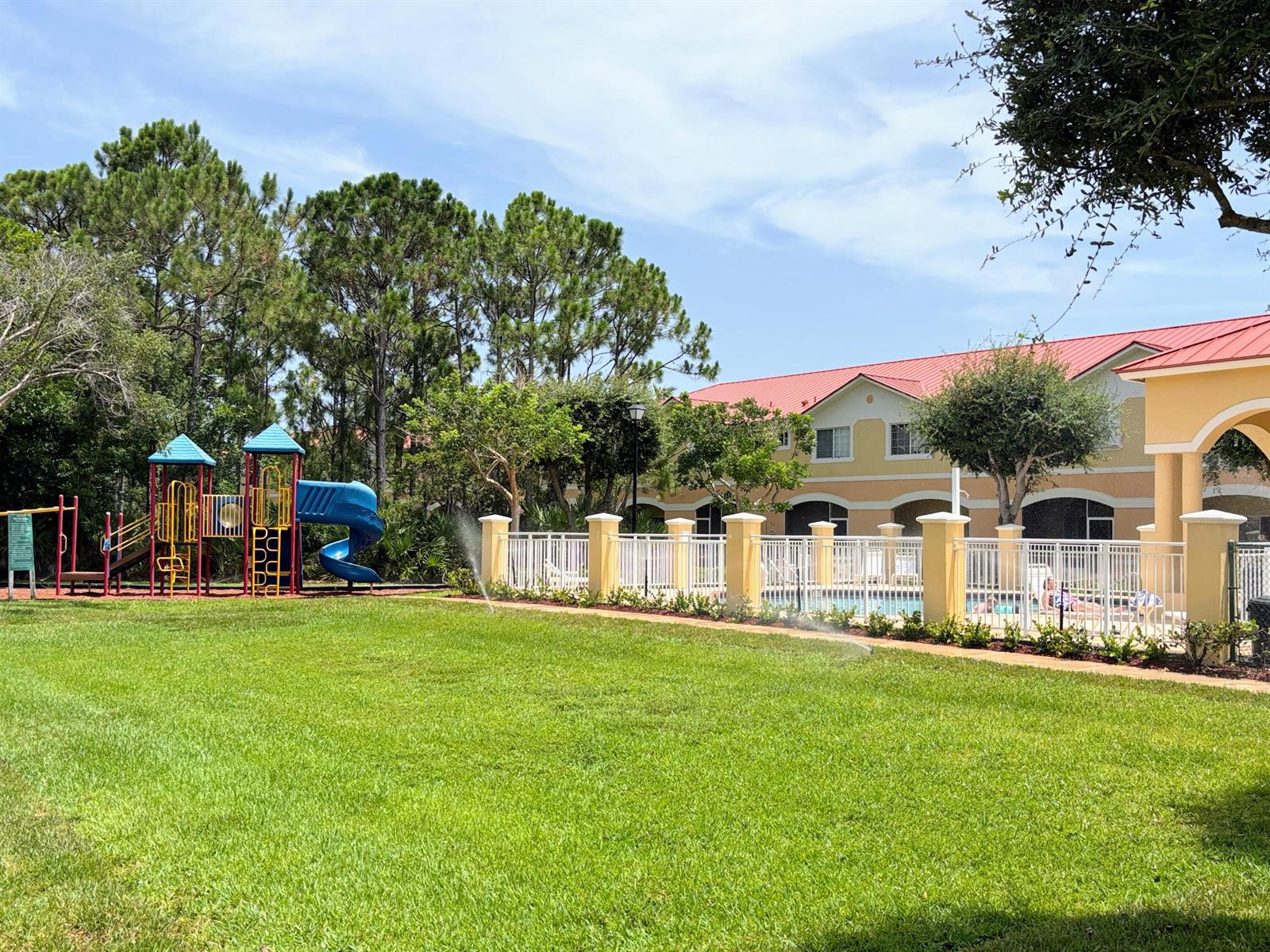 A playground and a fenced swimming pool area sit on a lawn near a building — 5088 SE Mariner Garden Circle, Stuart FL 34997, STUART, FL