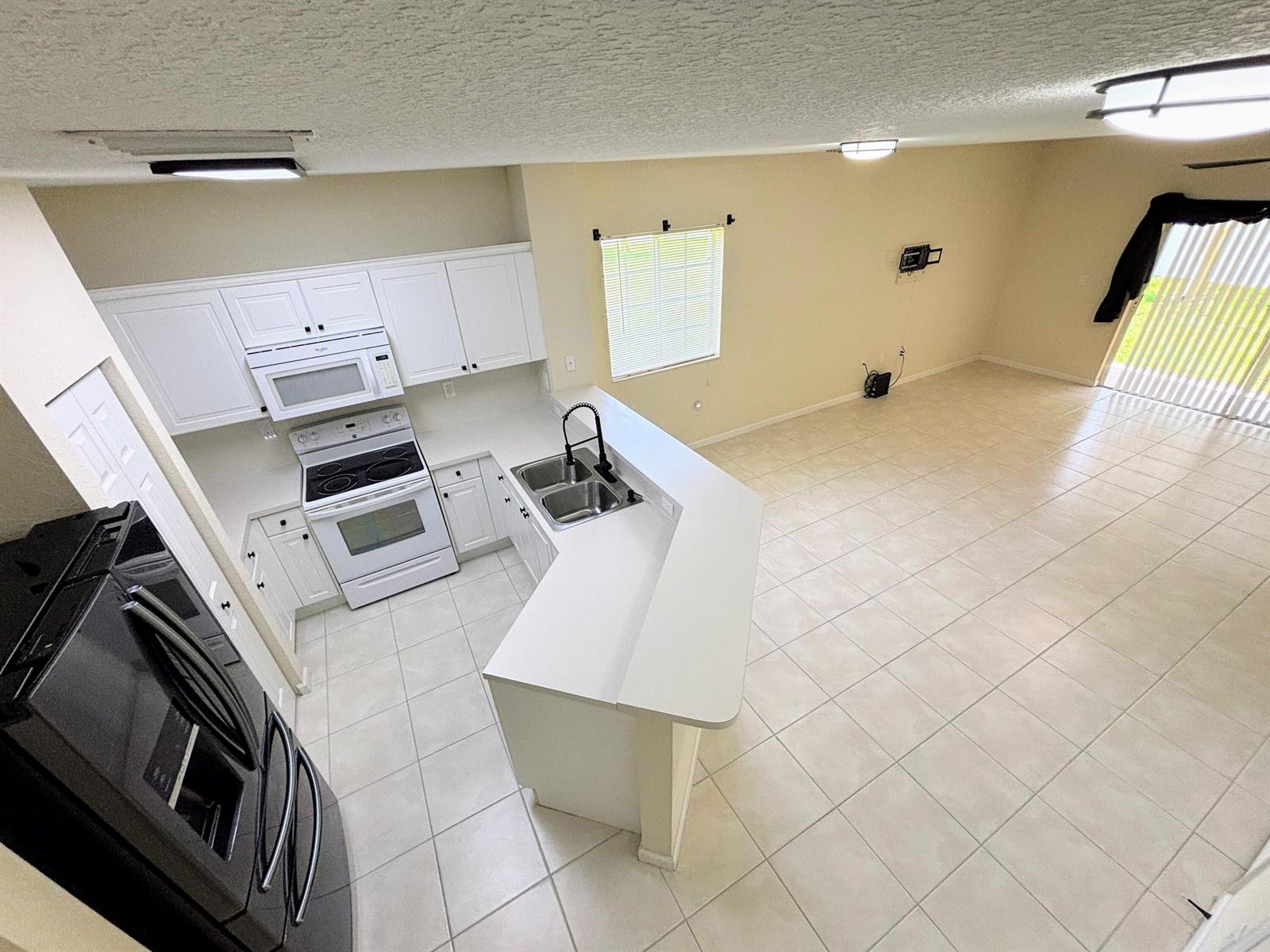 An elevated view of a kitchen with white cabinets, white appliances, and tiled flooring — 5088 SE Mariner Garden Circle, Stuart FL 34997, STUART, FL