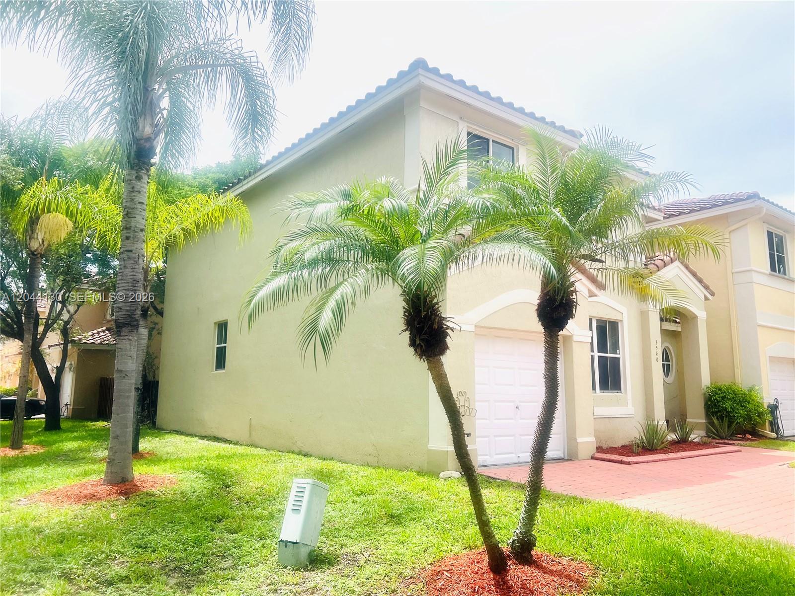 A two-story stucco house features a white garage door, palm trees, and a paved driveway — 3540 SW 170th Ave # 0, Miramar FL 33027, MIRAMAR, FL