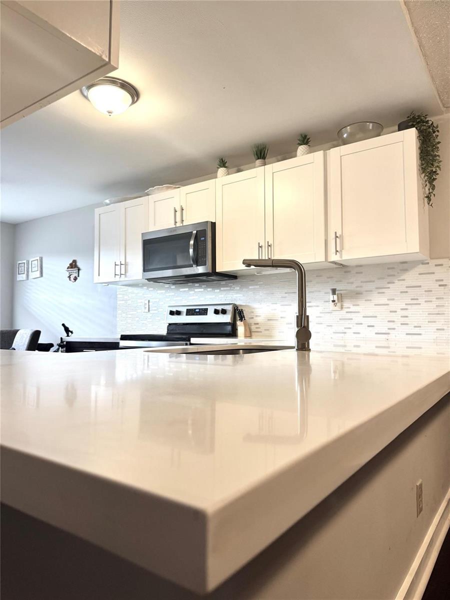 A kitchen features white cabinets, a quartz countertop, a stainless steel microwave, and tiled backsplash — 2704 NW 104th Avenue # 308, Sunrise FL 33322, SUNRISE, FL