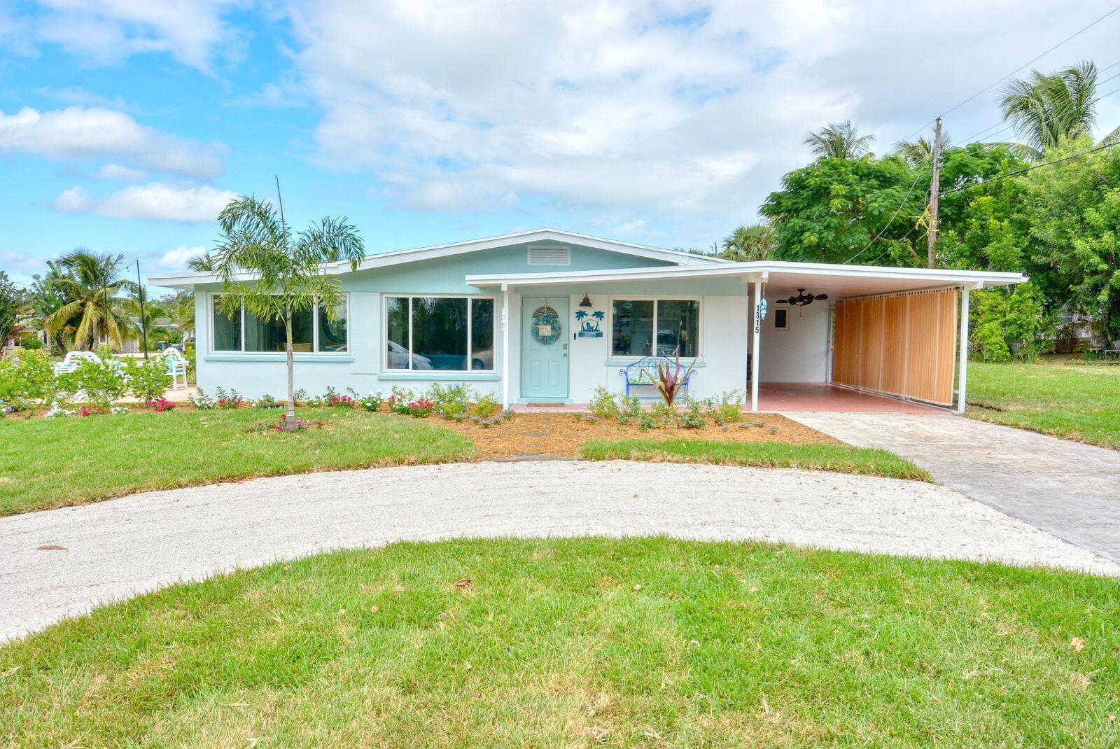 A light blue single-story house with a gravel driveway, carport, and landscaped front yard — 1315 NE Flora Place, Jensen Beach FL 34957, JENSEN BEACH, FL