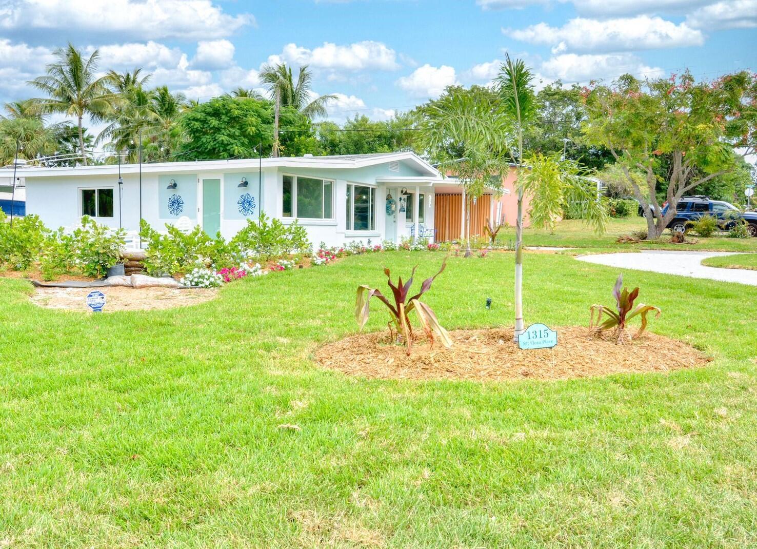 A single-story house with a light blue exterior, a green front door, and a landscaped lawn — 1315 NE Flora Place, Jensen Beach FL 34957, JENSEN BEACH, FL