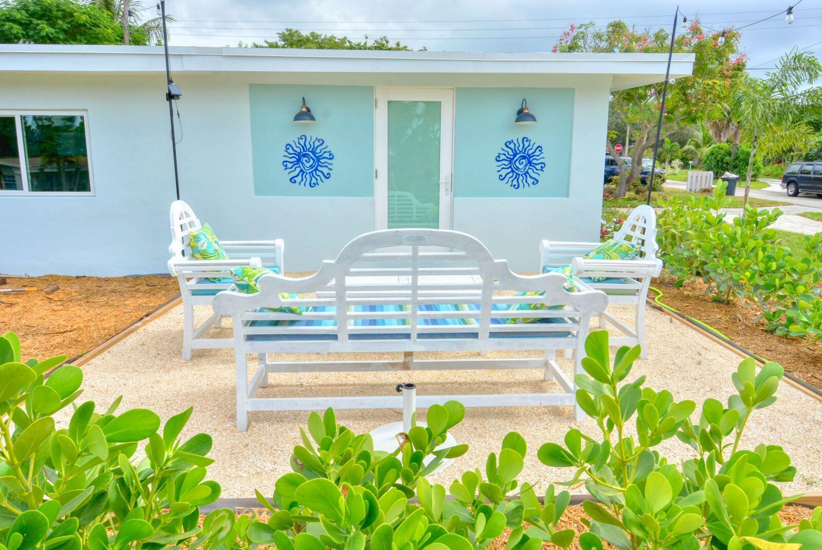 A white outdoor bench and two chairs sit on a gravel patio before a house — 1315 NE Flora Place, Jensen Beach FL 34957, JENSEN BEACH, FL