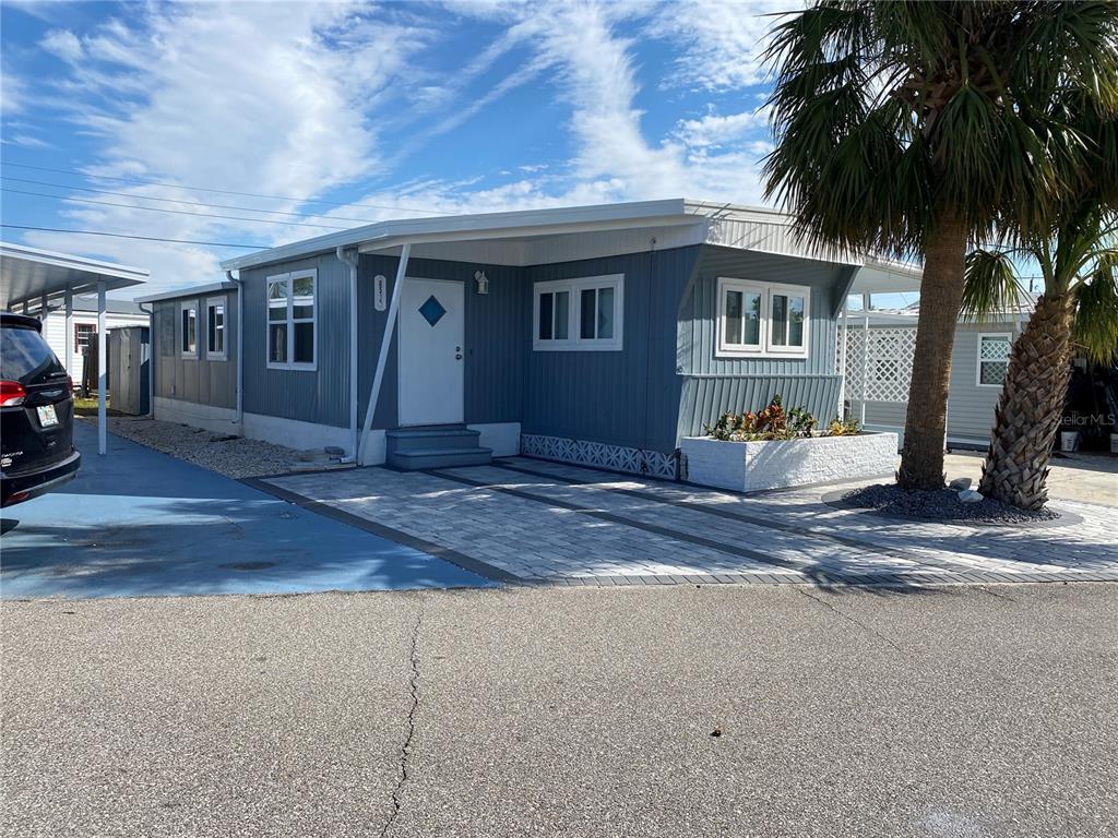 A blue mobile home with a white door, paved driveway, and a palm tree outside — 6517 ARIZONA STREET, BRADENTON, FL