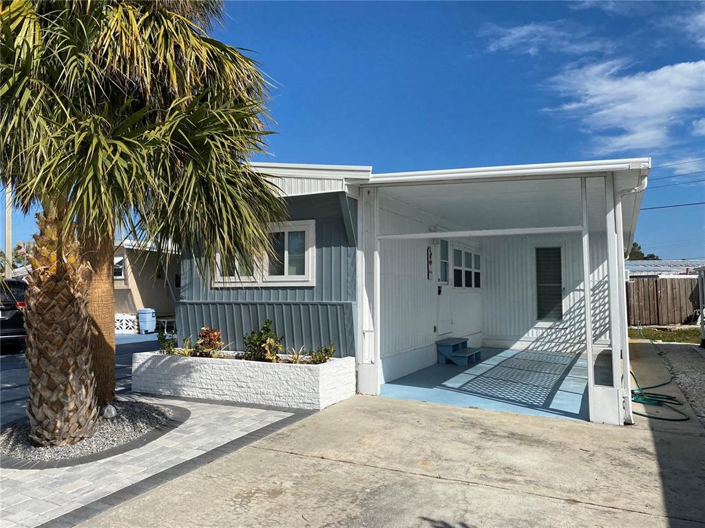 A single-story mobile home features a blue-grey facade, a white carport, and a palm tree — 6517 ARIZONA STREET, BRADENTON, FL