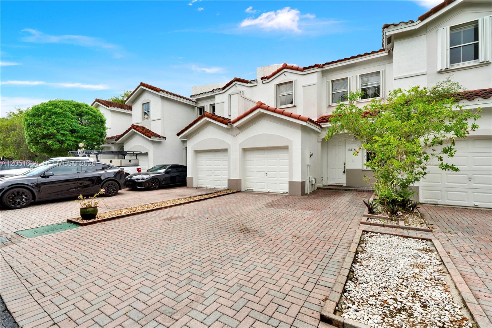 The exterior of a multi-unit townhouse complex features white stucco walls, red tile roofs, and brick-paved driveways — 11416 NW 43rd Ter, Doral FL 33178, DORAL, FL