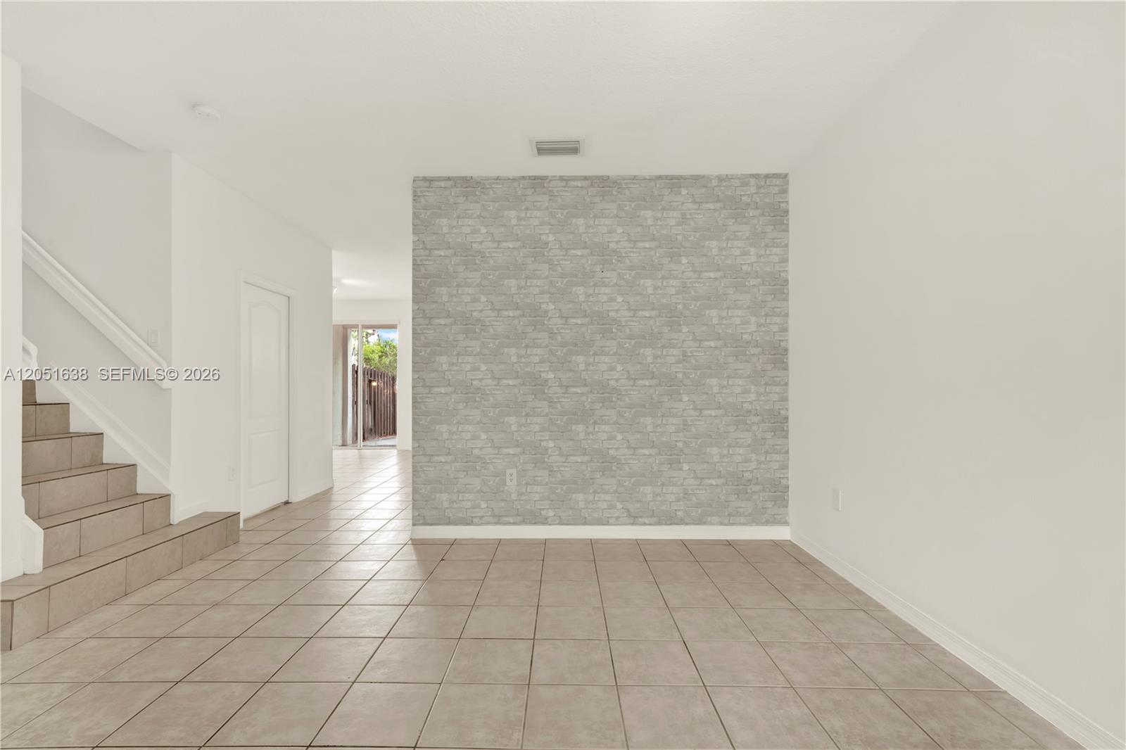 An empty room features light-colored tile flooring, a faux brick accent wall, and a staircase — 11416 NW 43rd Ter, Doral FL 33178, DORAL, FL
