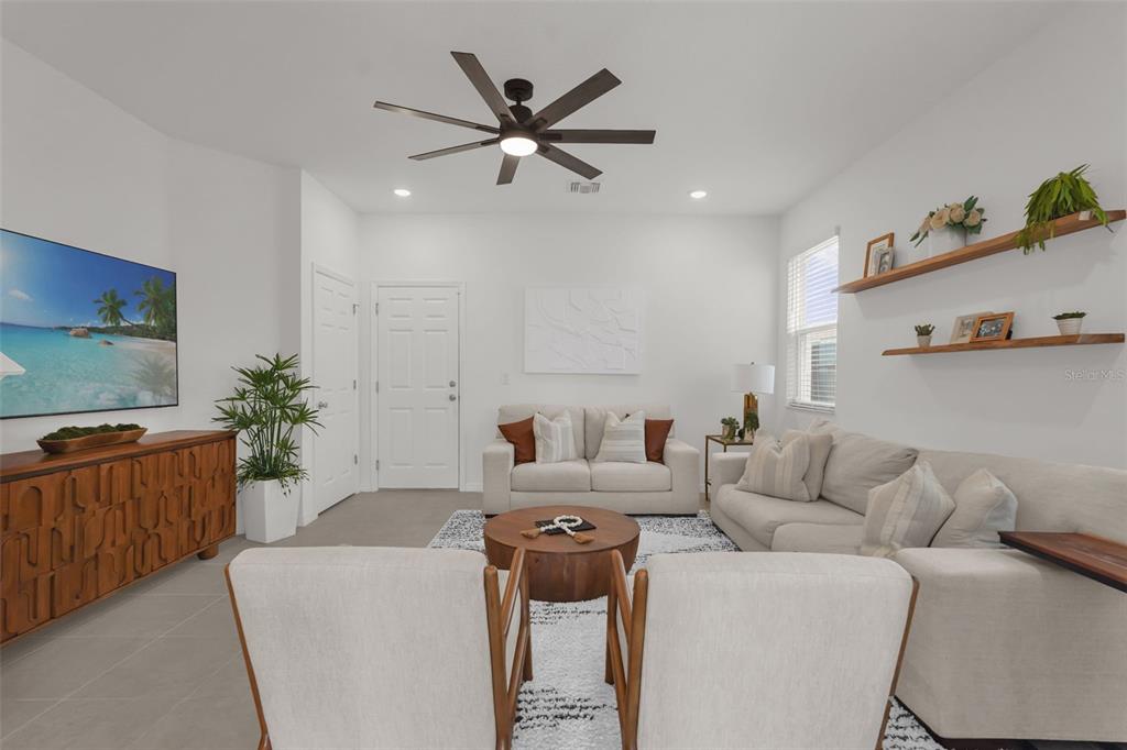 A living room features a ceiling fan, a sofa, two chairs, and wall-mounted wooden shelves — 1297 STOCKWELL AVENUE, ST CLOUD, FL