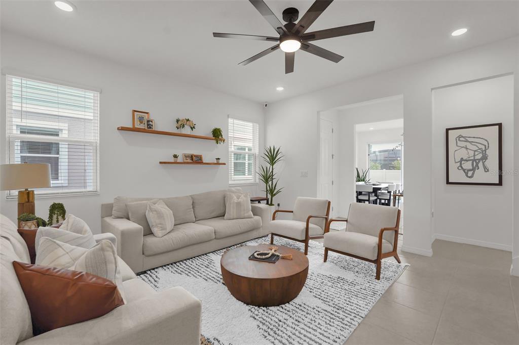 A bright living room features a light-colored sofa, two armchairs, a round coffee table, and shelving — 1297 STOCKWELL AVENUE, ST CLOUD, FL