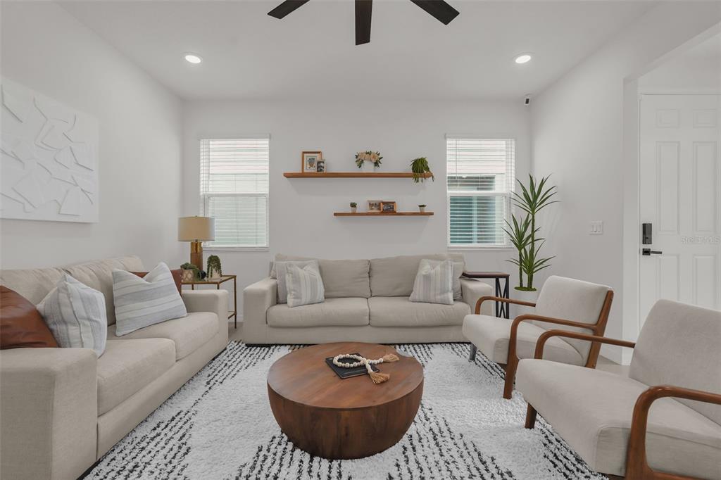 A living room features two beige sofas, two wooden armchairs, a round coffee table, and shelves — 1297 STOCKWELL AVENUE, ST CLOUD, FL
