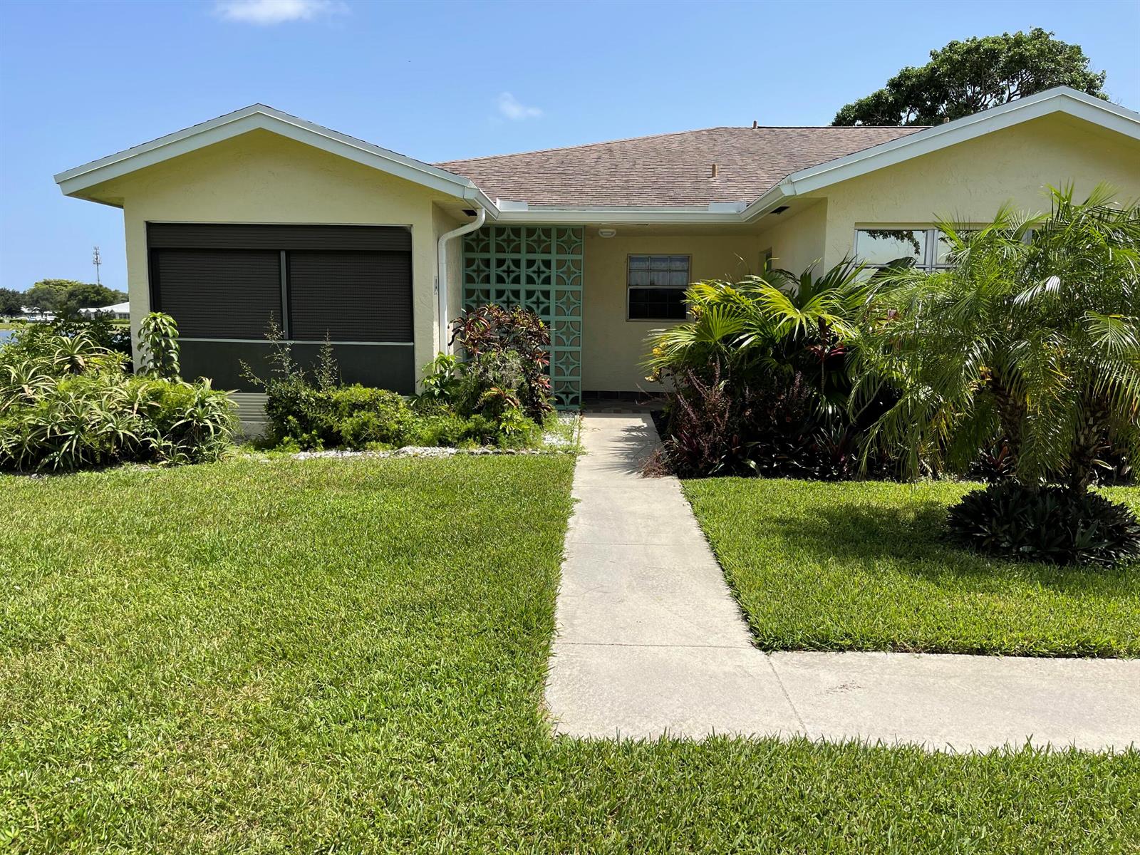 A single-story yellow house features a concrete walkway, a decorative breeze block wall, and landscaping — 5360 Lakefront Boulevard # A, Delray Beach FL 33484, DELRAY BEACH, FL