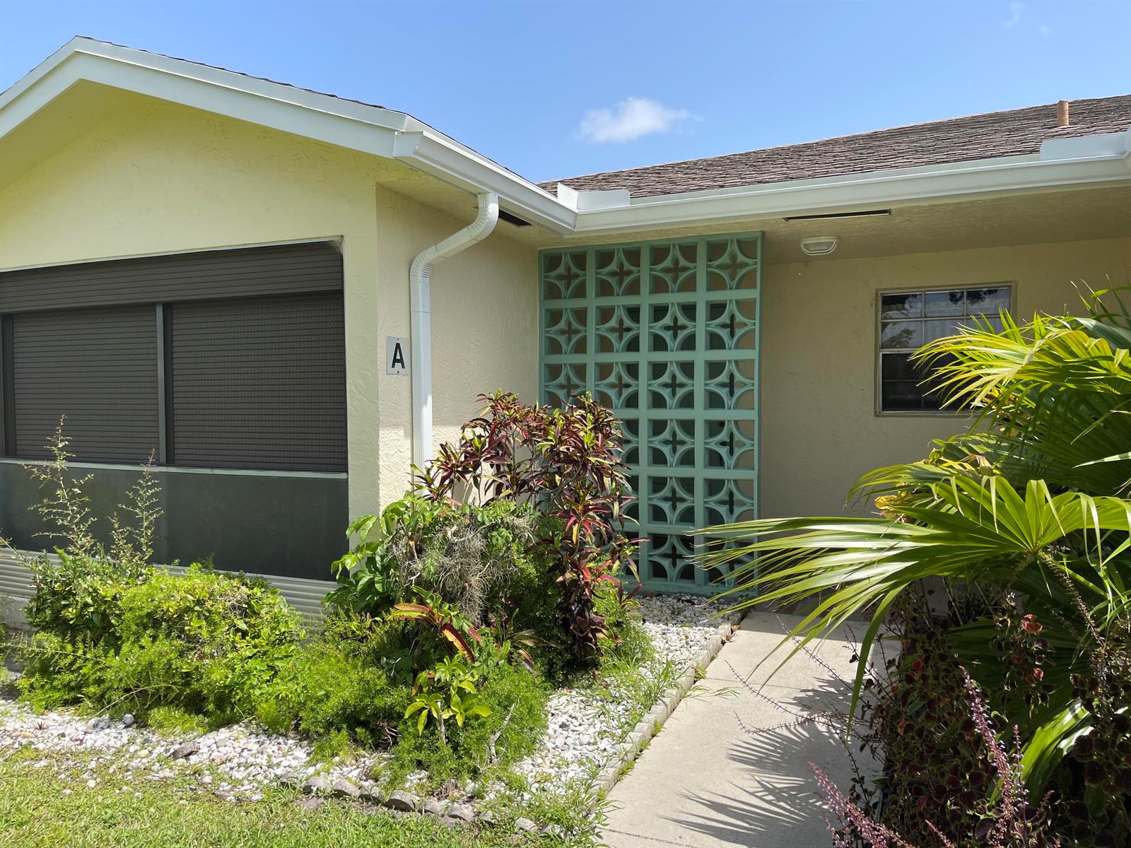 The exterior of a yellow house features a decorative teal breeze block privacy screen — 5360 Lakefront Boulevard # A, Delray Beach FL 33484, DELRAY BEACH, FL