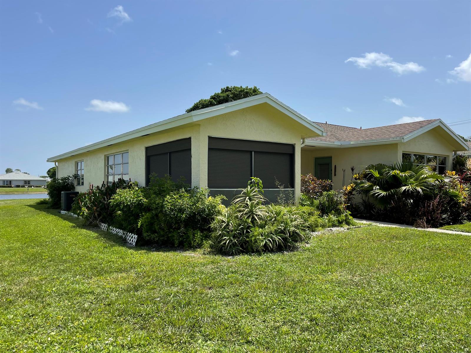 A yellow single-story house with a screened-in porch and lush landscaping under a blue sky — 5360 Lakefront Boulevard # A, Delray Beach FL 33484, DELRAY BEACH, FL