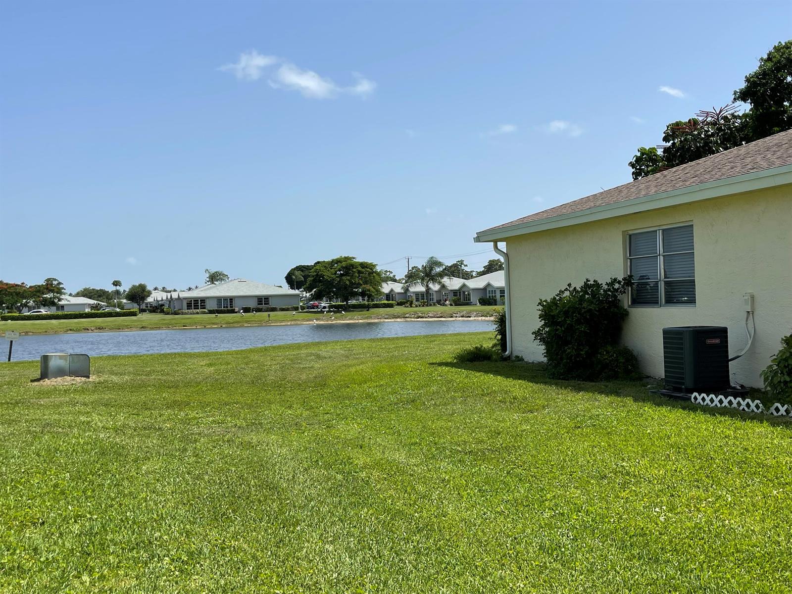 A view of a grassy backyard, a pond, and neighboring houses under a blue sky — 5360 Lakefront Boulevard # A, Delray Beach FL 33484, DELRAY BEACH, FL
