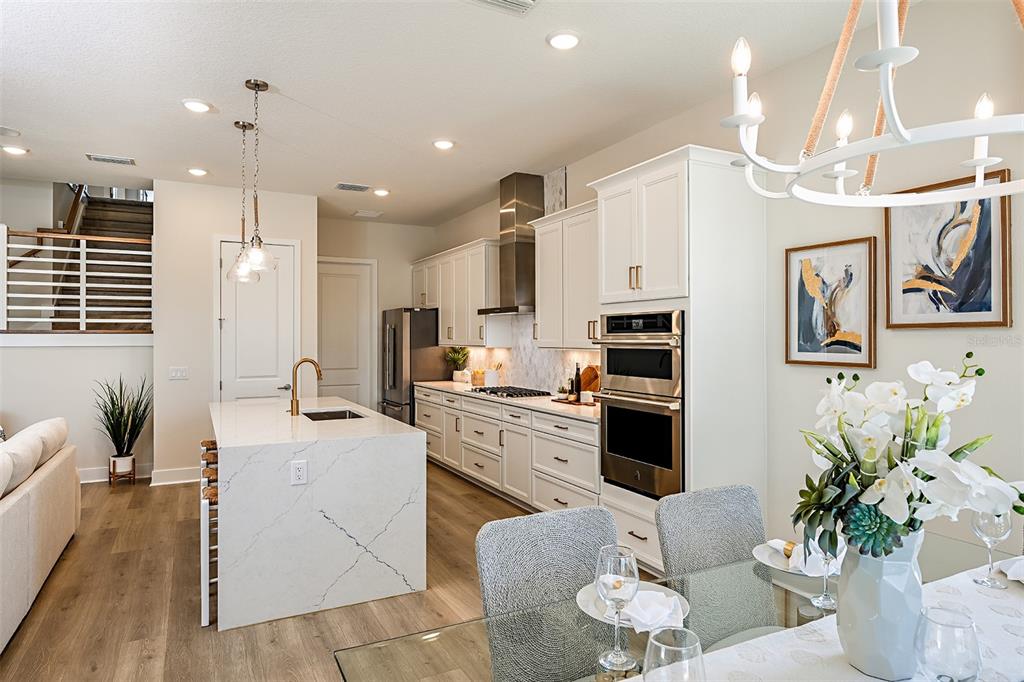 A modern kitchen features white cabinetry, a quartz island, stainless steel appliances, and wood flooring — 719 MALDIVES TRAIL, SARASOTA, FL