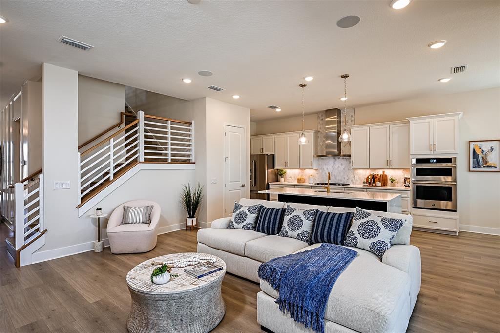 An open-concept living room and kitchen featuring a sectional sofa, staircase, and white cabinetry — 719 MALDIVES TRAIL, SARASOTA, FL