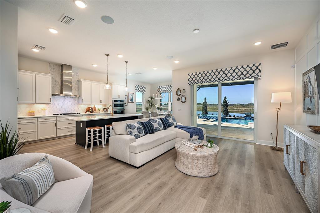 An open-concept living room and kitchen featuring light wood floors, a sectional sofa, and pool views — 719 MALDIVES TRAIL, SARASOTA, FL