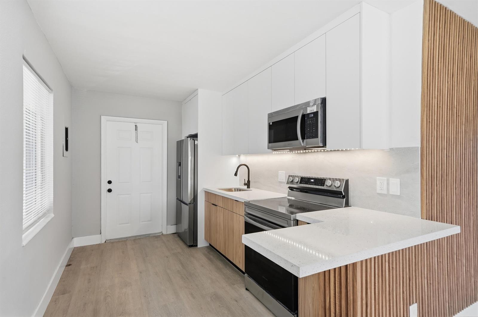 A modern kitchen features white upper cabinets, wood-tone lower cabinets, stainless steel appliances, and countertops — 2625 NW 10th Street, Pompano Beach FL 33069, POMPANO BEACH, FL
