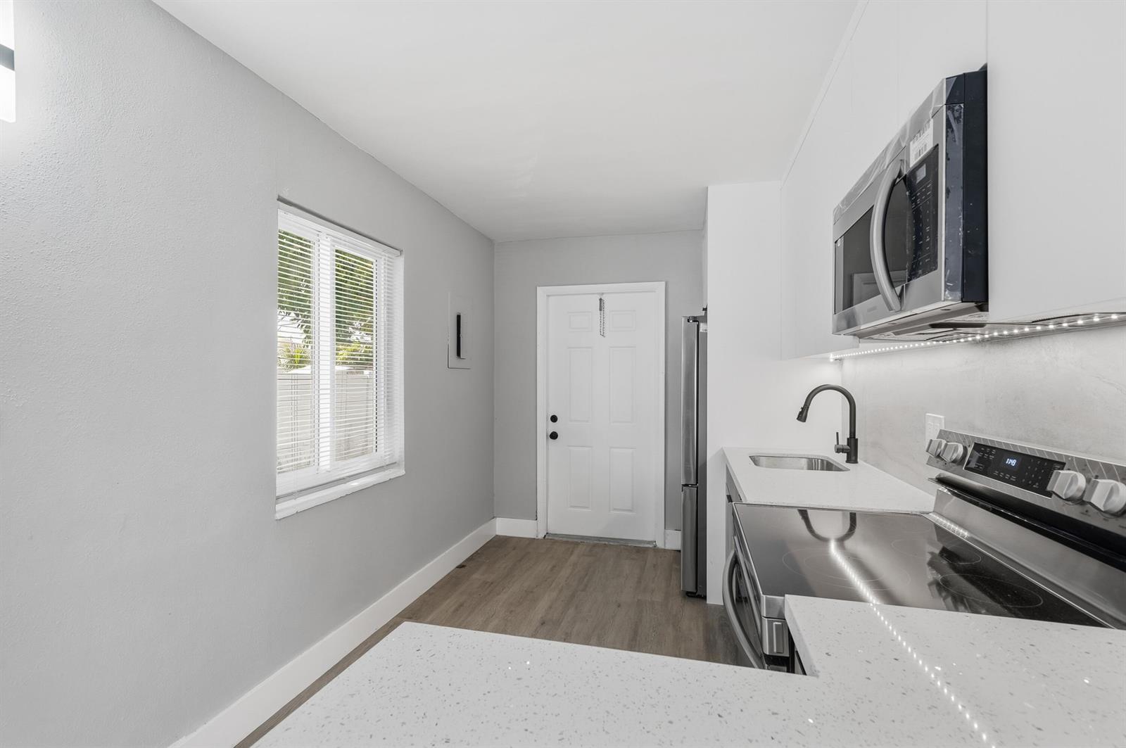 A modern kitchen features white cabinets, quartz countertops, stainless steel appliances, and light wood flooring — 2625 NW 10th Street, Pompano Beach FL 33069, POMPANO BEACH, FL