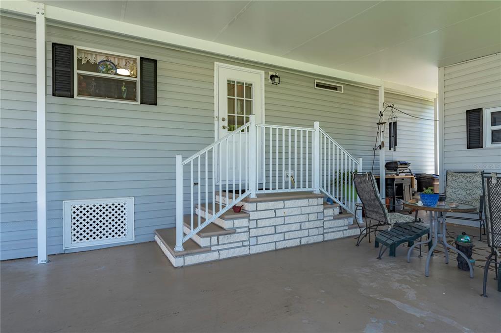 A covered patio features light blue siding, a white door with stairs, and outdoor furniture — 1000 KINGS HIGHWAY UNIT 133, PORT CHARLOTTE, FL