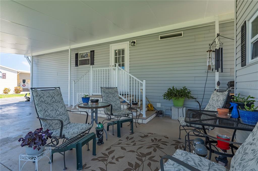 A covered patio features outdoor furniture, a patterned rug, and stairs leading to a house entrance — 1000 KINGS HIGHWAY UNIT 133, PORT CHARLOTTE, FL