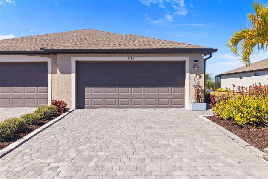 A paved driveway leads to a two-car garage with brown doors on a stucco house — 2145 BONITO WAY, PORT CHARLOTTE, FL