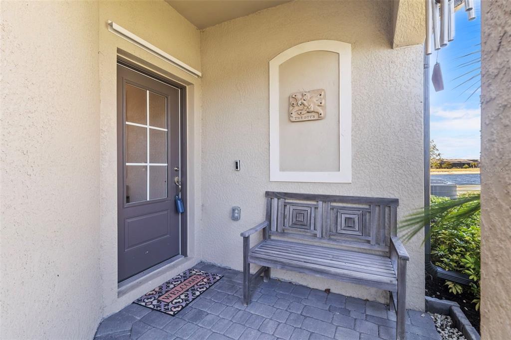 A covered entryway features a gray front door, a wooden bench, and a welcome mat — 2145 BONITO WAY, PORT CHARLOTTE, FL