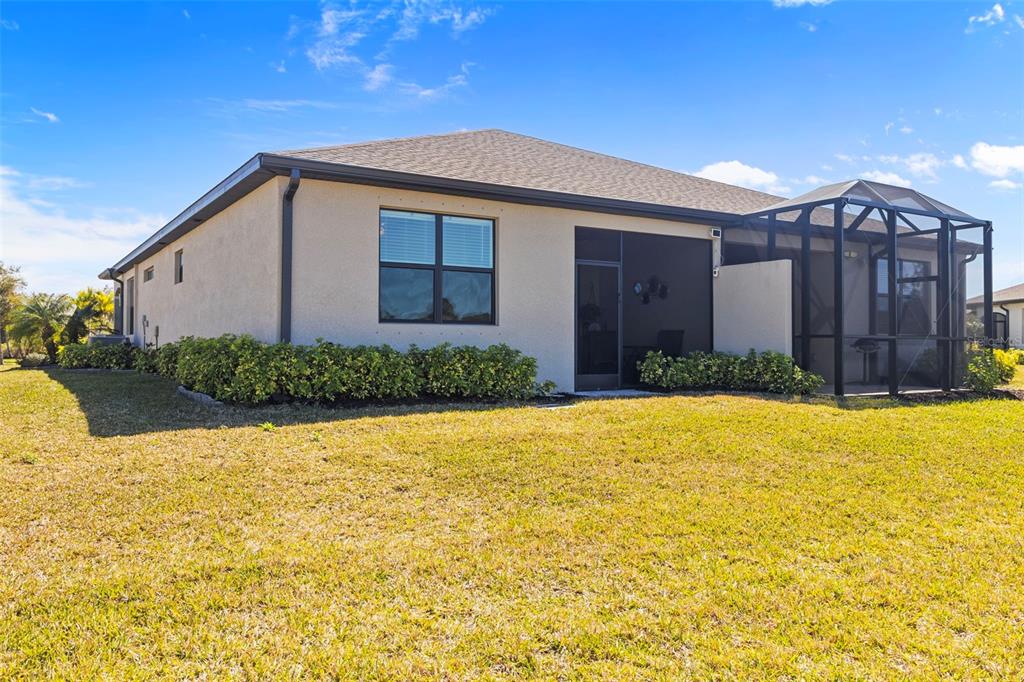 The rear exterior of a single-story house features a screened-in lanai and landscaped bushes — 2145 BONITO WAY, PORT CHARLOTTE, FL