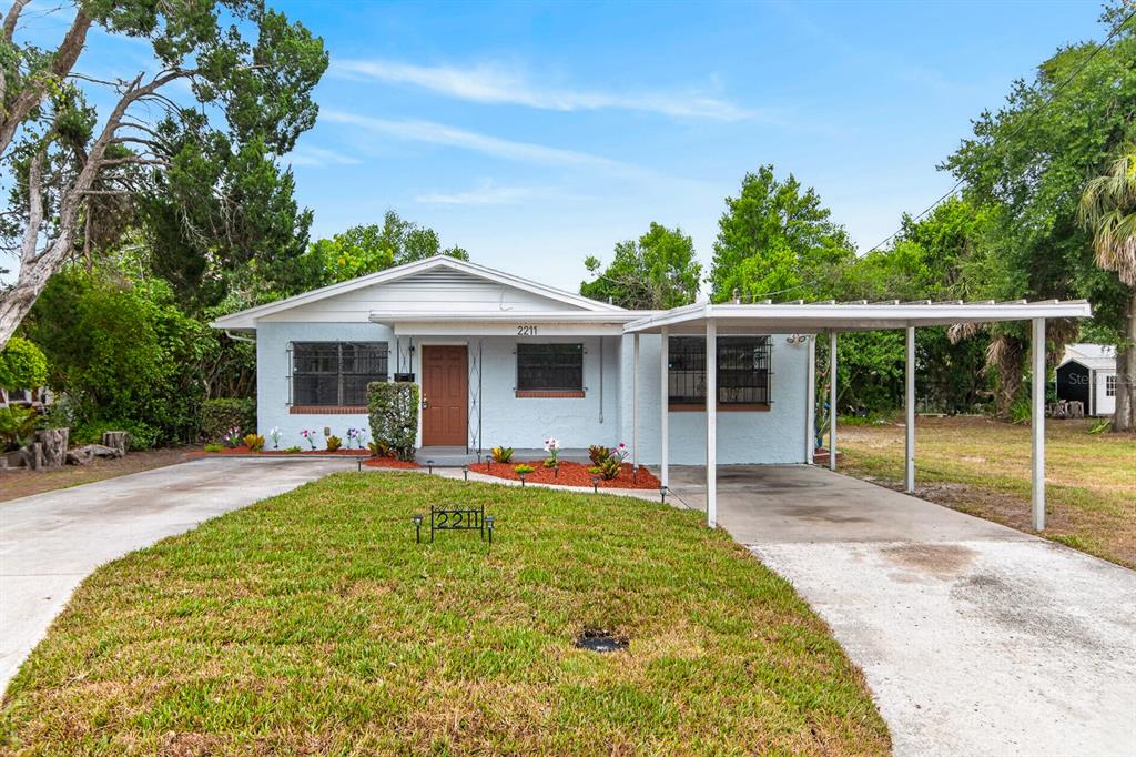 A single-story house with a light blue exterior, a front carport, and a grassy lawn — 2211 MALLORY AVENUE, TAMPA, FL