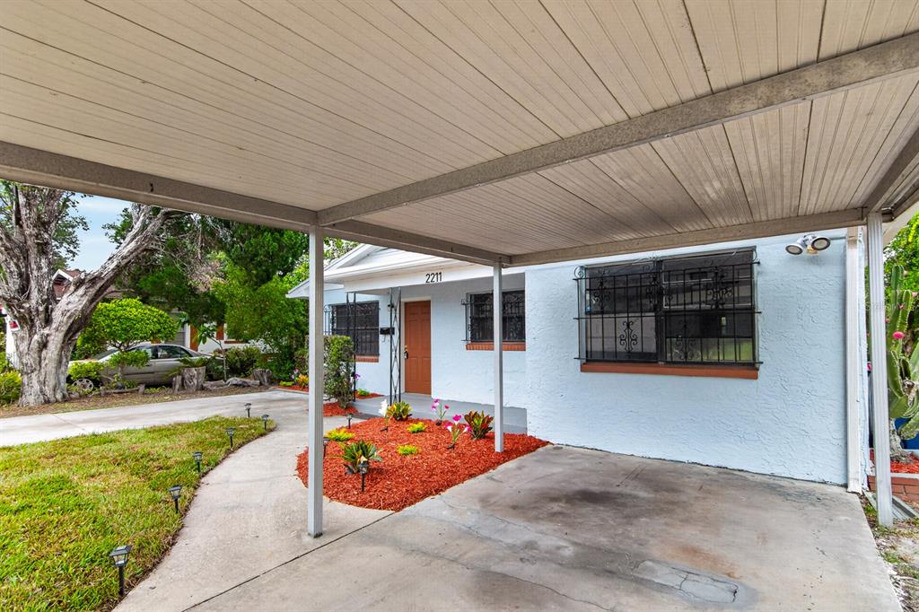 A light blue house features a concrete driveway, a metal carport, and a small garden — 2211 MALLORY AVENUE, TAMPA, FL