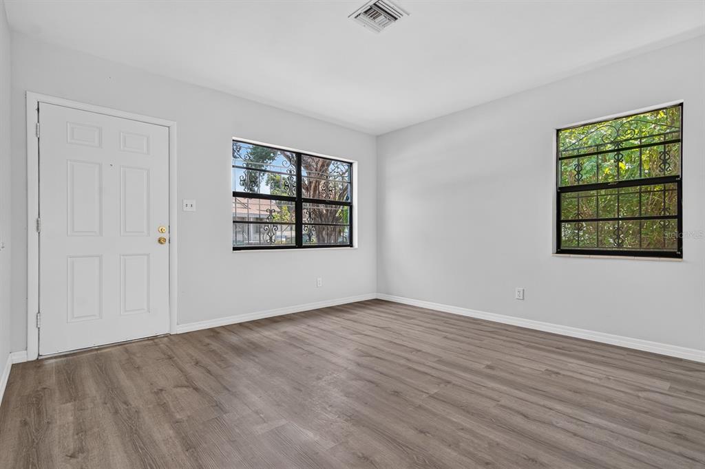 An empty room features light gray walls, wood-look flooring, two windows with security bars, and a door — 2211 MALLORY AVENUE, TAMPA, FL
