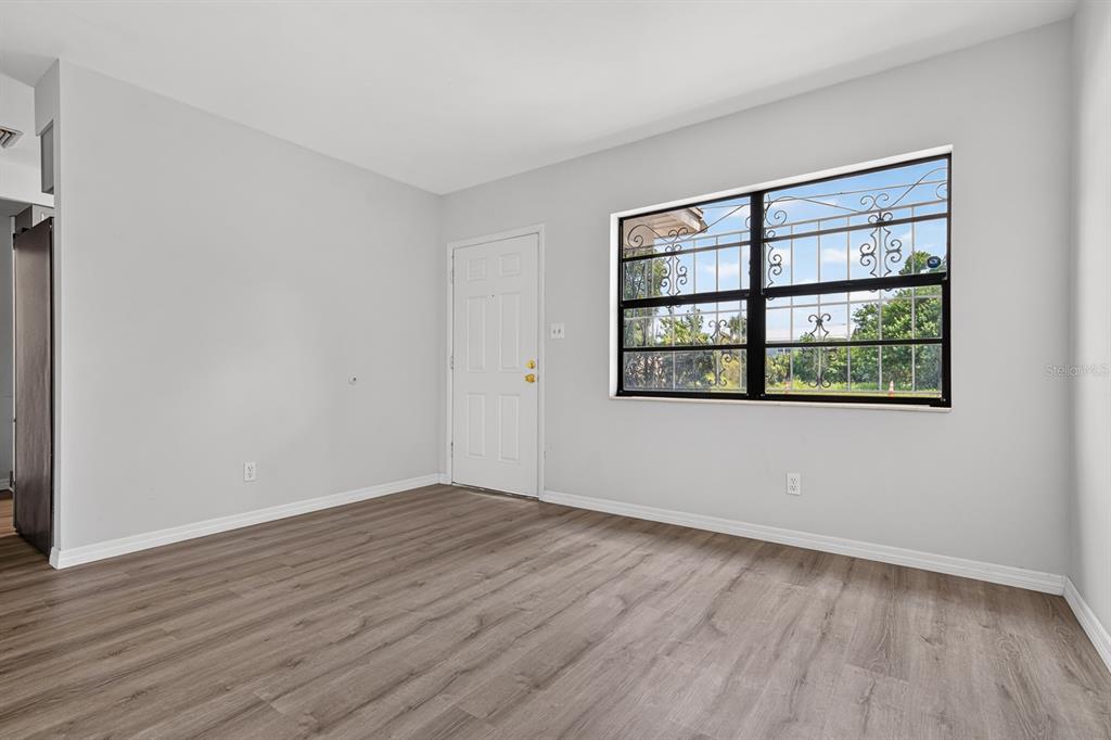 An empty room with light gray walls, wood-look flooring, a white door, and a barred window — 2211 MALLORY AVENUE, TAMPA, FL