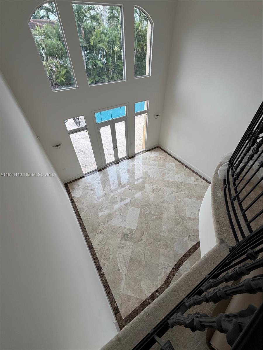 A high-ceilinged foyer features marble tile flooring, a curved staircase, and large arched windows — 673 Destacada Ave, Coral Gables FL 33156, CORAL GABLES, FL