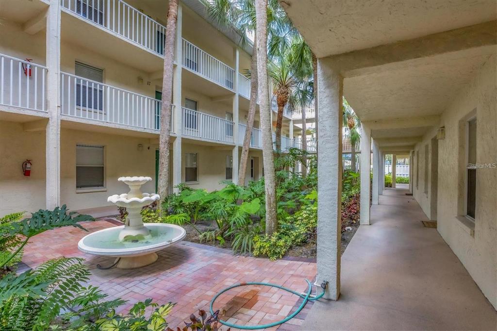 A courtyard features a tiered fountain, lush tropical landscaping, and a covered walkway — 7294 CLOISTER DRIVE UNIT 9, SARASOTA, FL