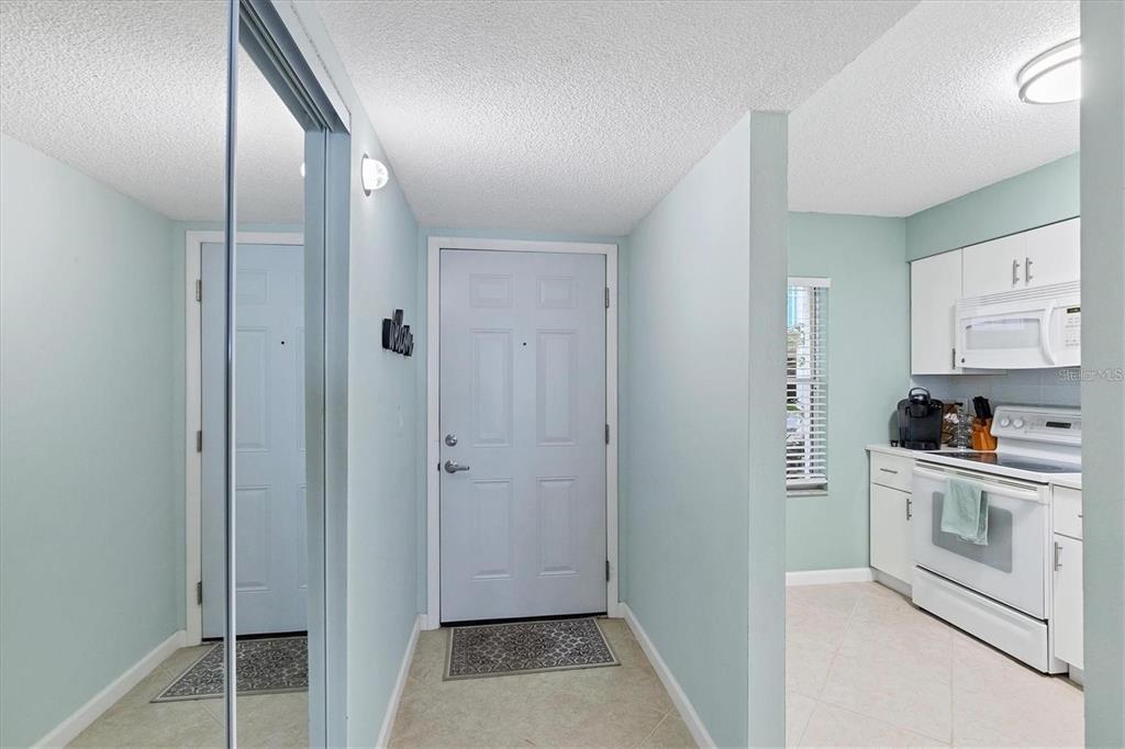 An entryway with a white door, mirrored closet, and an adjacent kitchen with white cabinets — 7294 CLOISTER DRIVE UNIT 9, SARASOTA, FL