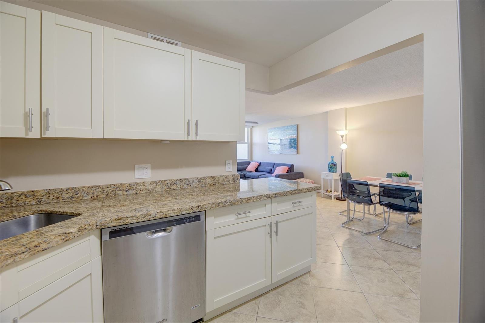 A kitchen with white cabinets and granite countertops overlooks a dining area and living room — 305 N Pompano Beach Boulevard # 1403, Pompano Beach FL 33062, POMPANO BEACH, FL