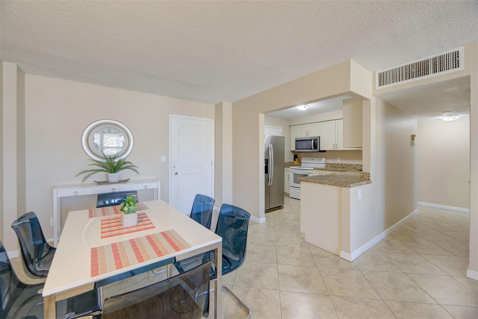 A dining area with a white table and blue chairs sits adjacent to a kitchen — 305 N Pompano Beach Boulevard # 1403, Pompano Beach FL 33062, POMPANO BEACH, FL