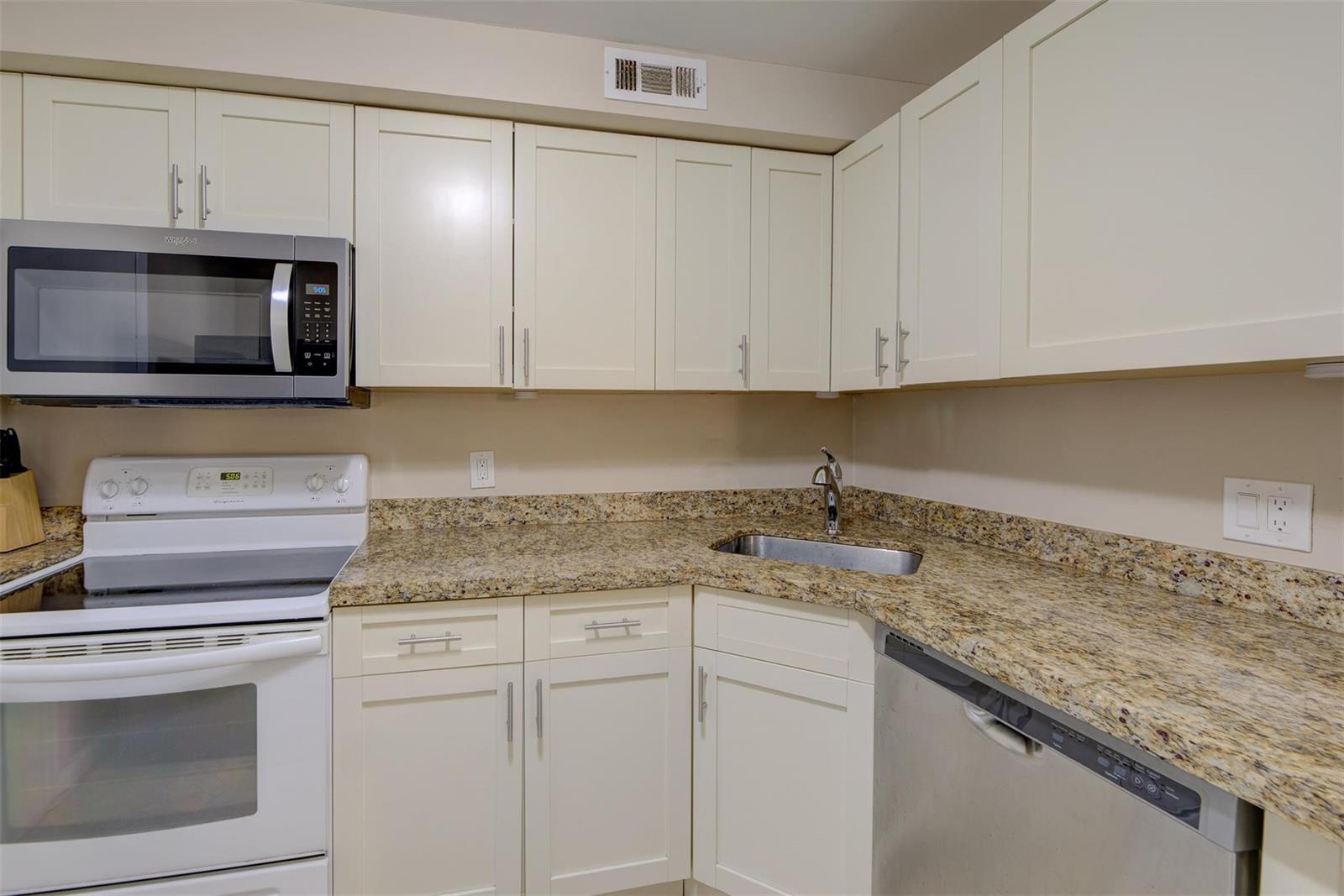A kitchen features off-white cabinets, granite countertops, a stainless steel sink, and white appliances — 305 N Pompano Beach Boulevard # 1403, Pompano Beach FL 33062, POMPANO BEACH, FL