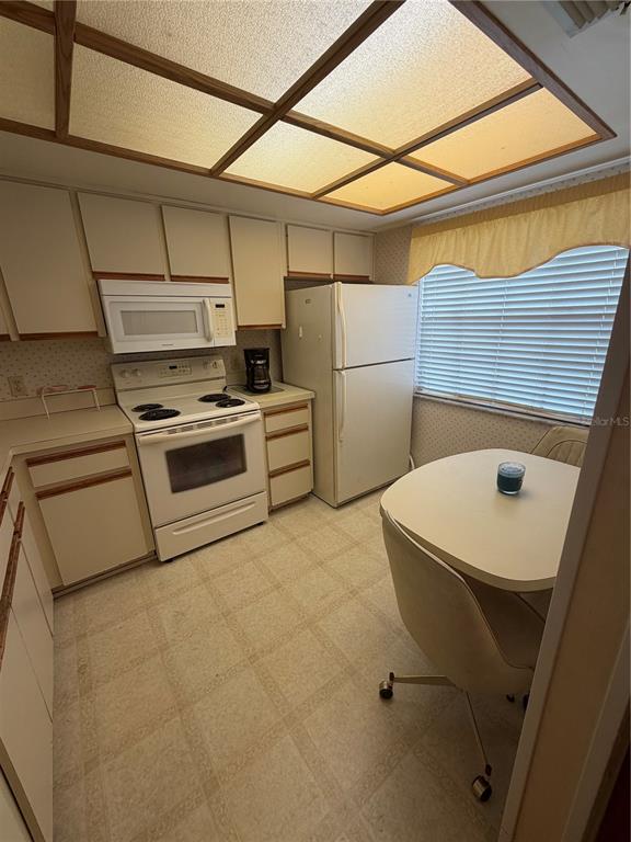 A kitchen features white appliances, light-colored cabinets, a small dining table, and a grid ceiling — 2400 WINDING CREEK BOULEVARD UNIT 18A-110, CLEARWATER, FL